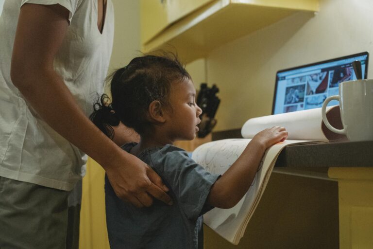 A mother assists her young child with homework at home using digital resources.