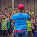 A volunteer guides a diverse group of children in an outdoor activity, fostering community spirit and teamwork.