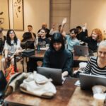 Diverse group of adults in a collaborative office meeting, actively engaged with laptops and discussion.